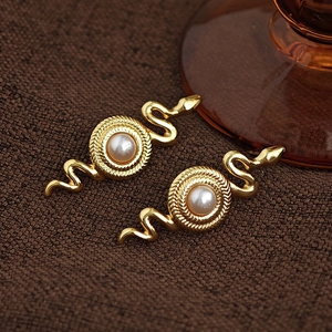 Makro-Detail von schlangenförmigen goldenen Ohrringen mit Perle auf strukturiertem Stoff
