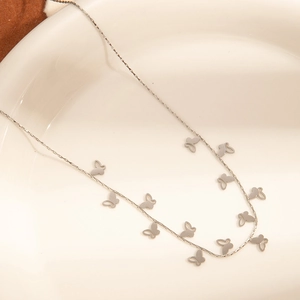 Detail of silver stainless steel necklace with butterfly charms on a white ceramic plate