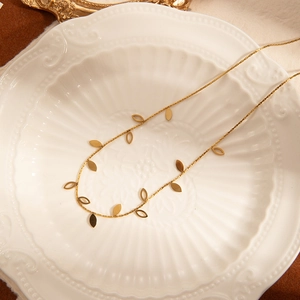 Detail of a gold leaf necklace with hollow and solid charms on a vintage ceramic plate