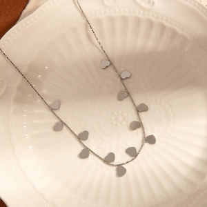 Detailed view of silver stainless steel necklace with delicate heart sequins on white ceramic