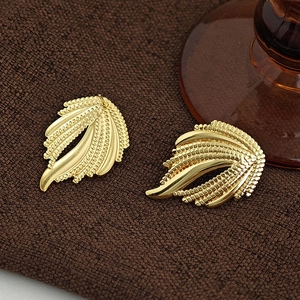 Detailaufnahme goldener Federohrringe mit feiner Perlenstruktur auf braunem Stoffhintergrund