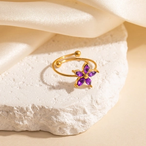 Detail of gold floral ring with purple drop-shaped crystals on stone and satin background