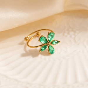 Detail of gold floral ring with five green teardrop stones on white ceramic plate