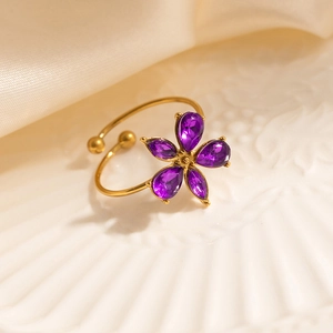 Detailed close-up of a gold-plated flower ring with purple gems on white ceramic