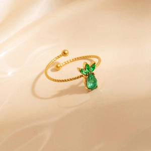Golden pineapple ring with green zircons on a wavy beige fabric background
