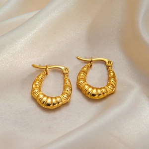 Macro detail of golden twist earrings on champagne silk showing smooth texture