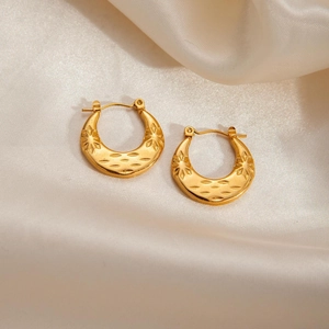 Detail view of gold twist hoop earrings with vintage star engraving on silk background