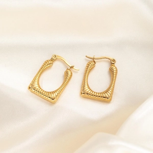 Detailed view of gold twisted metal hoop earrings on elegant white silk background