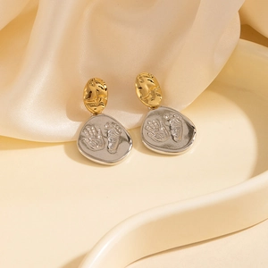 Détail de boucles d'oreilles bicolores avec empreintes de bébé en relief sur métal