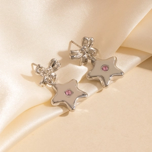 Détail de boucles d'oreilles nœud argenté avec étoile et pierre rose sur de la soie