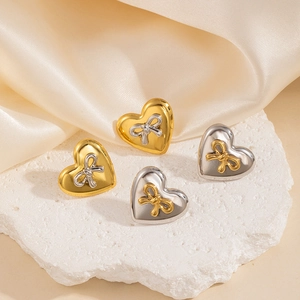 Dettaglio macro degli orecchini a cuore con fiocco metallico in finitura bicolore oro e argento