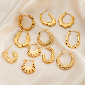 Collection of textured gold titanium steel hoop earrings on white silk fabric background