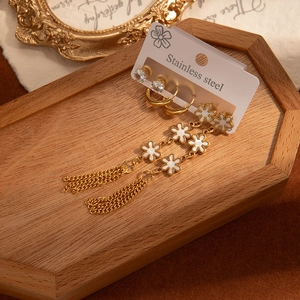 Détail d'un ensemble de boucles d'oreilles en acier doré avec pompons fleurs et puces