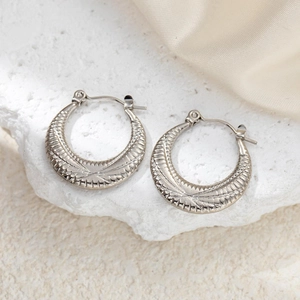 Silver crescent hoop earrings with geometric stripes on a white marble background