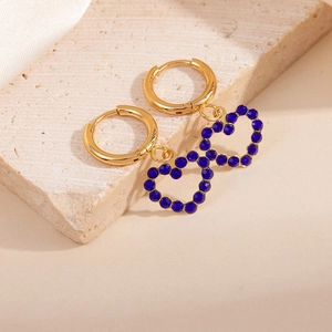 Goldene hohle Herzohrringe mit blauen Zirkonias auf Stein- und Seidenhintergrund