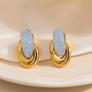 Boucles d'oreilles dorées géométriques avec texture marbre bleu sur fond de soie élégant