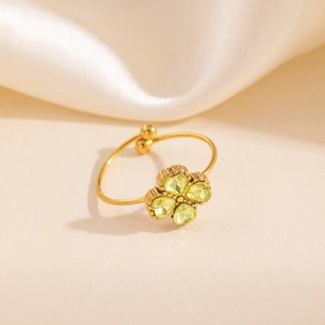 Gros plan d'une bague trèfle dorée avec zircons verts en forme de cœur sur soie