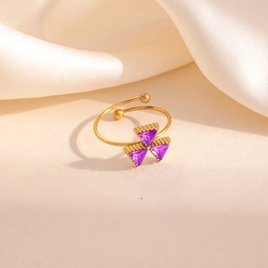 Détail d'une bague trèfle dorée avec pierres de zircon violettes sur du satin blanc