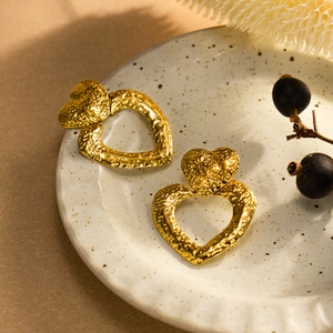 Goldene Herz-Ohrhänger mit Hammerschlag-Textur präsentiert in einer Keramikschale