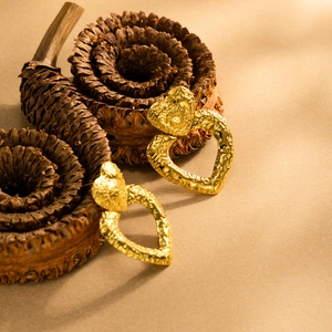 Goldene Herzohrringe mit gehämmerter Lavastruktur auf Vintage Trockenblumen