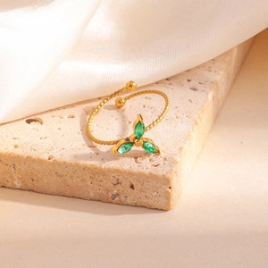 Détail d'une bague torsadée dorée avec des pierres de zircon vert sur un socle en pierre beige