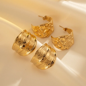 Detail view of gold chunky C-shape earrings with hammered and wavy textures on satin fabric