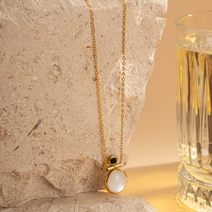 Detail of 18k gold plated necklace with white cat eye stone and green accent on a rock