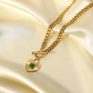 Collar vintage de corazón dorado con gema verde y cierre en T sobre fondo de seda champán