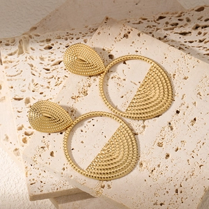Detail of gold-plated drop earrings with hammered dot texture on travertine stone background