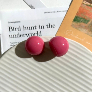Dettaglio di orecchini a sfera in resina fucsia su vassoio bianco con texture