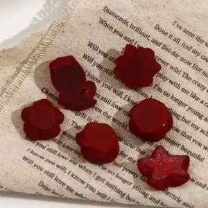 DIY burgundy resin charms in flower and star shapes on a vintage fabric background