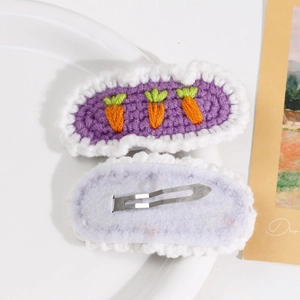 Detail of handmade purple knitted hair clips featuring orange carrot embroidery