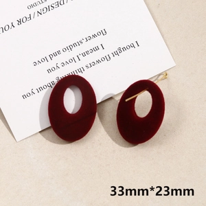Detailed view of burgundy velvet oval drop earrings with gold hooks on beige texture
