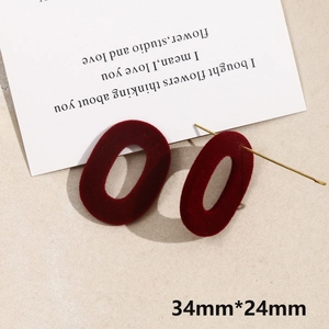 Macro shot of 34x24mm wine red flocked oval earrings with golden pins on beige texture