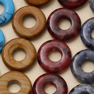 Makroaufnahme bunter Naturstein-Donutperlen mit einzigartigen Mineraltexturen für DIY-Schmuck