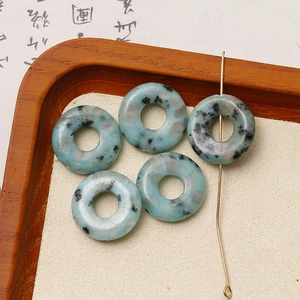 Detailansicht von fünf Naturstein-Donut-Perlen mit blauen Fleckenmustern in Holzschale