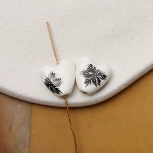 Macro shot of heart-shaped white ceramic bead with black leaf pattern for DIY jewelry