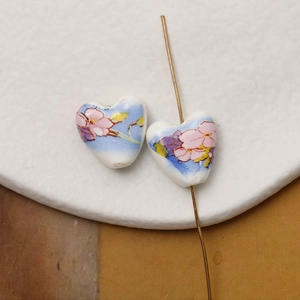 Macro detail of hand-painted heart-shaped ceramic beads with floral patterns and vertical holes