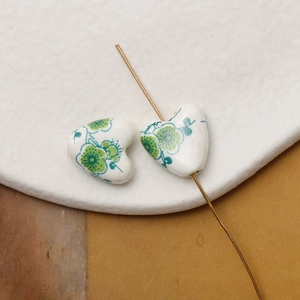 Detailed macro view of heart-shaped white ceramic beads with hand-painted green floral patterns