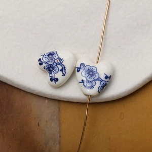 Macro detail of heart-shaped ceramic beads with blue floral patterns and gold pin