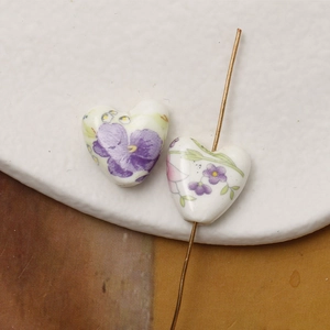 Macro detail of heart-shaped ceramic beads with hand-painted floral patterns and drill holes