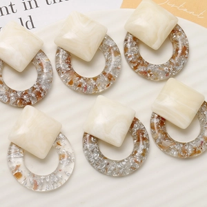 Detail of resin geometric earrings with marble texture and silver foil on ceramic tray