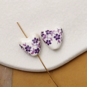 Macro detail of heart-shaped ceramic beads with purple floral patterns for DIY jewelry