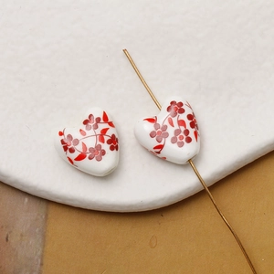Macro shot of heart-shaped ceramic beads with red flower patterns and gold needles