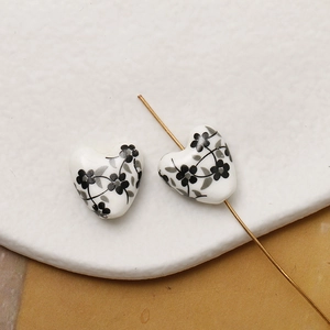 Macro shot of heart-shaped ceramic beads with hand-painted floral patterns and golden needle