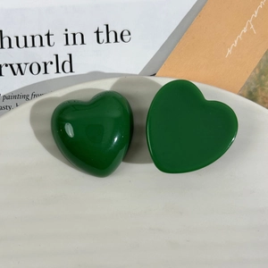 Detail of dark green glossy resin heart charms on a white ceramic plate for DIY jewelry