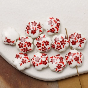 Macro shot of white flower ceramic beads with hand-painted red plum floral patterns