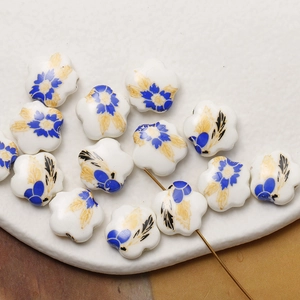 Close-up of hand-painted white ceramic flower beads with blue and gold floral patterns