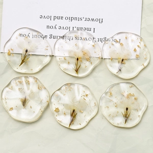Macro view of transparent resin oval charms with dry white flowers and gold foil flakes