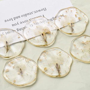 Close-up of clear resin charm with delicate white dried flowers and gold foil flakes